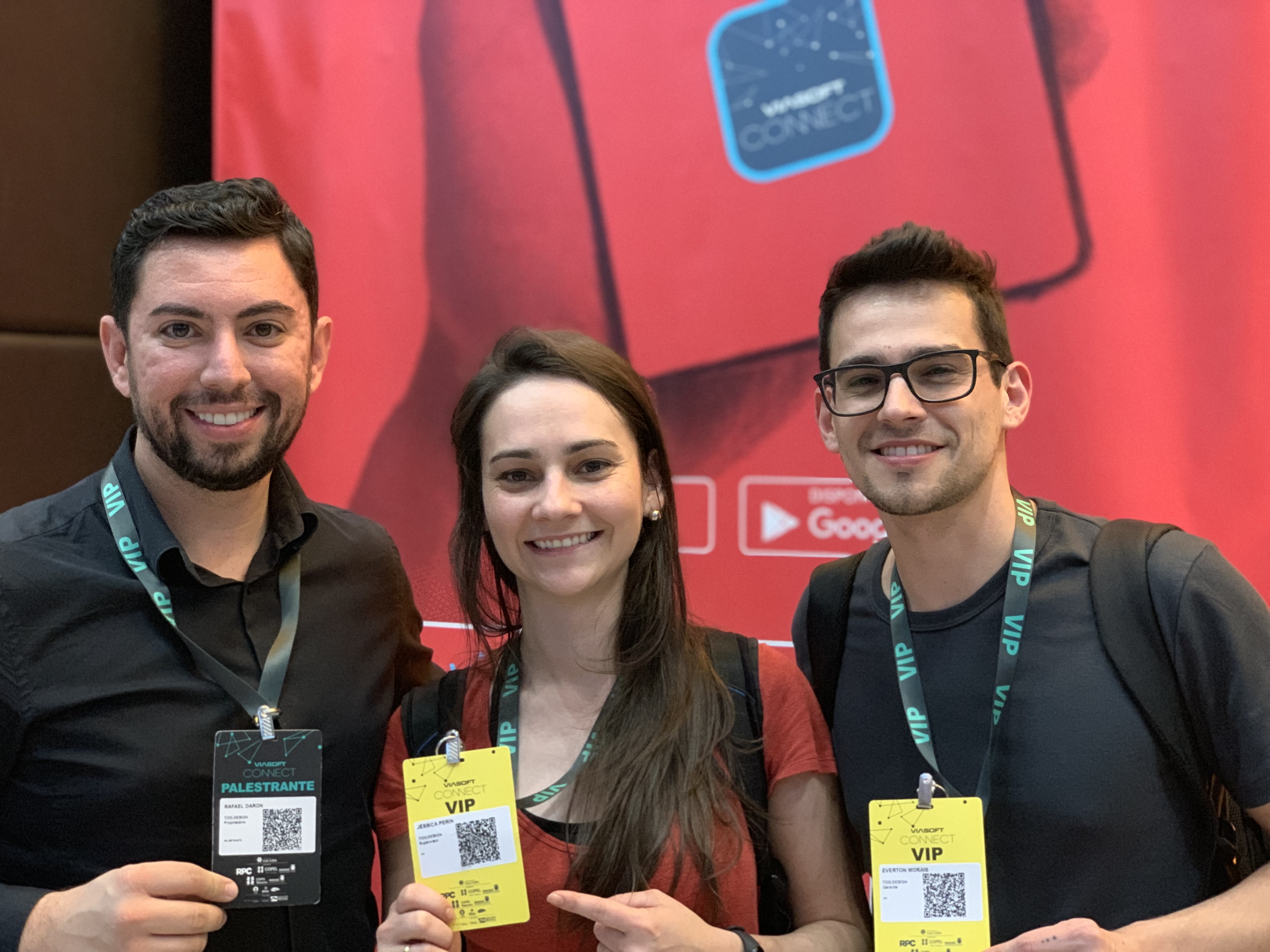 Event participants showing their speaker and VIP badges. Three people smiling and holding ID badges. The person on the left is a speaker, while the other two have VIP badges. The background is a red event banner.
