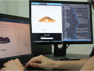 Person developing a product design website. Person working on a laptop and a monitor. The monitor displays a product design website and programming code.