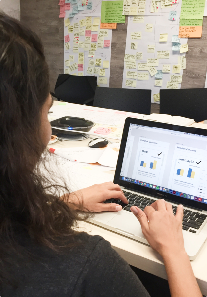 Person working on a prototype in Figma in a collaborative work environment. Person working on a laptop at an office table. The laptop displays a prototype in Figma. The background wall is covered with colorful post-it notes with annotations.