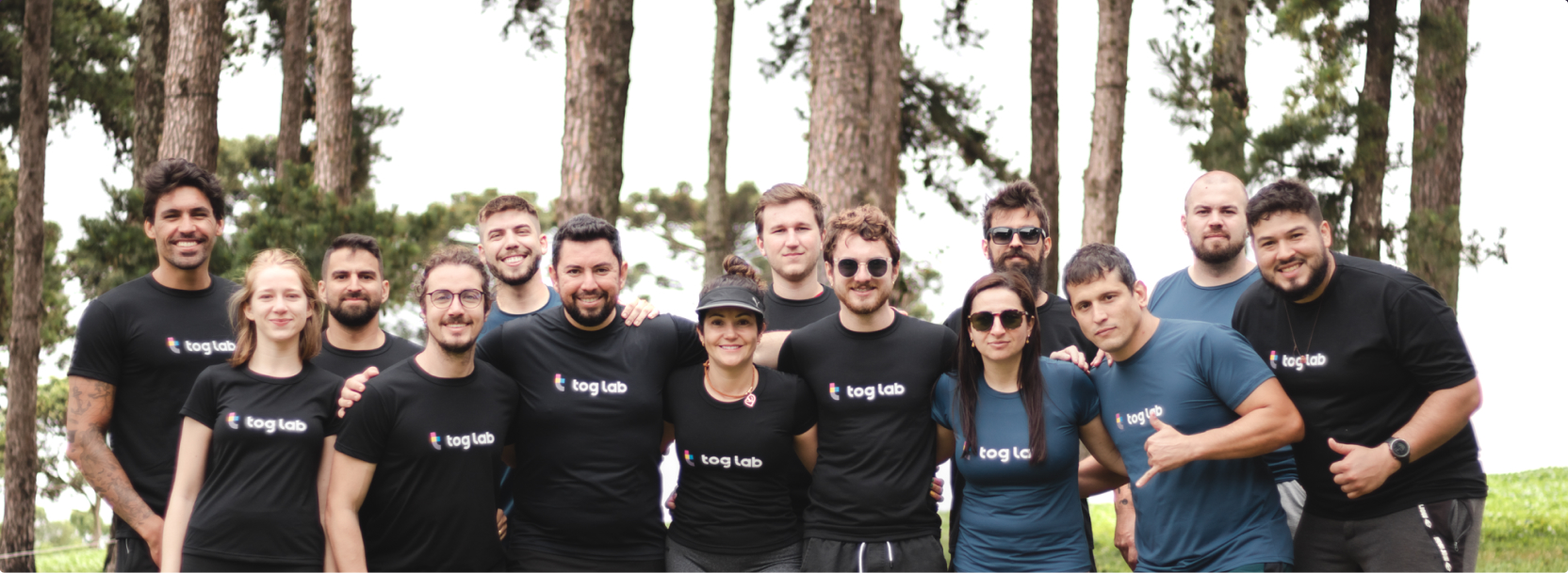 Tog lab team in an outdoor activity. A group of fifteen people, all wearing black shirts with the tog lab logo, posing together outdoors in a wooded area.