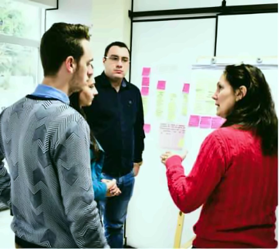 Quattro persone in piedi che parlano davanti a una lavagna bianca con post-it